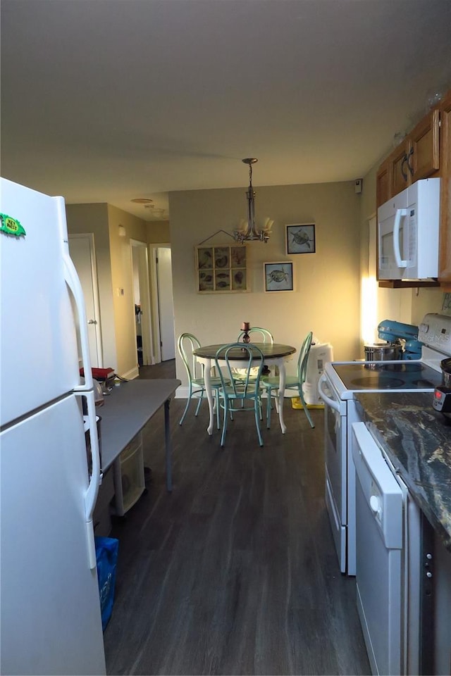 kitchen featuring dark hardwood / wood-style flooring, hanging light fixtures, white appliances, and dark stone counters