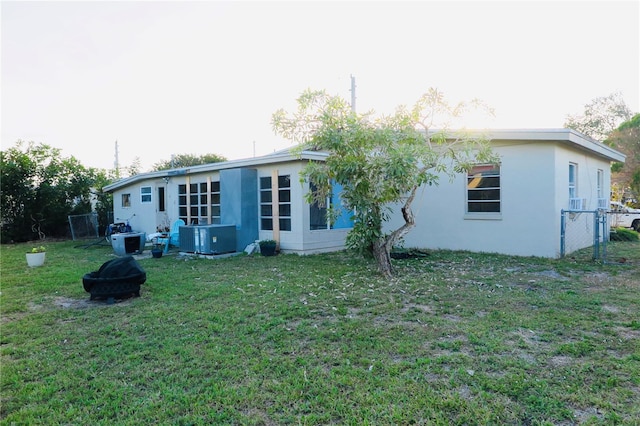 rear view of property with central AC, an outdoor fire pit, and a yard