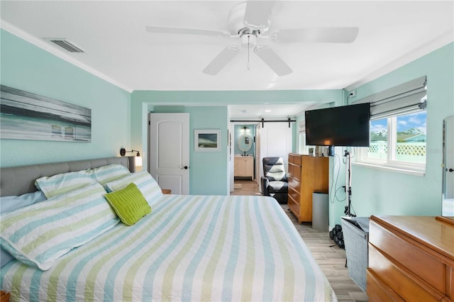 bedroom featuring crown molding, ceiling fan, connected bathroom, light hardwood / wood-style floors, and a barn door