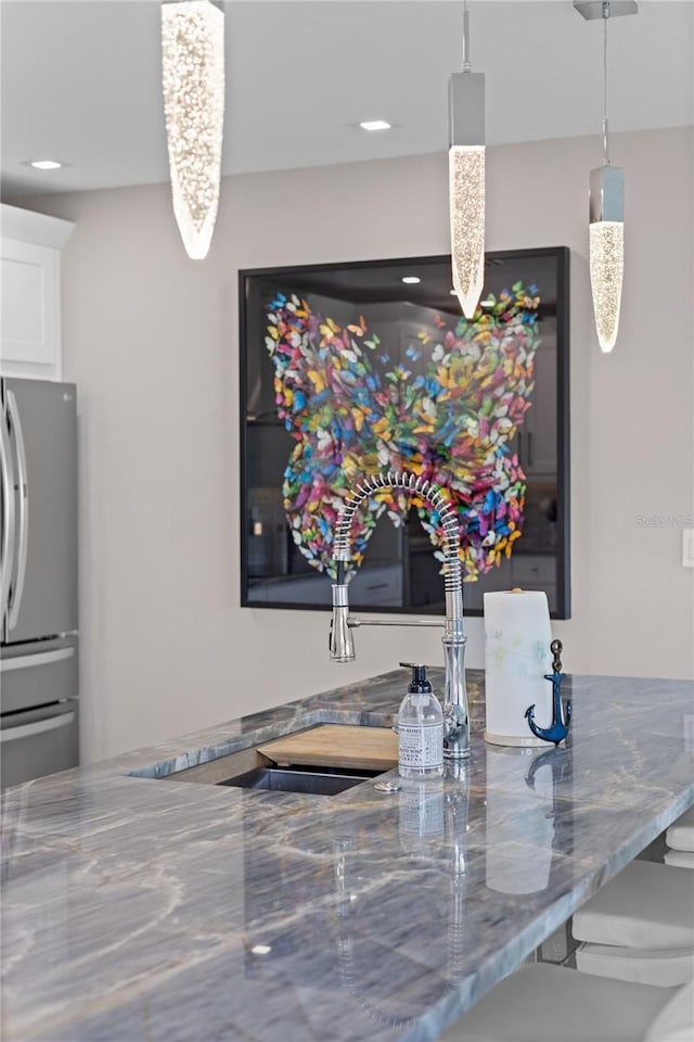 kitchen featuring white cabinetry, decorative light fixtures, stainless steel refrigerator, and stone counters