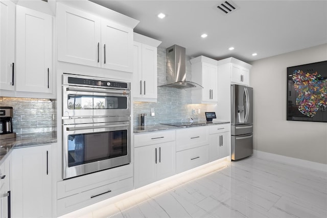 kitchen with appliances with stainless steel finishes, white cabinetry, dark stone countertops, decorative backsplash, and wall chimney exhaust hood