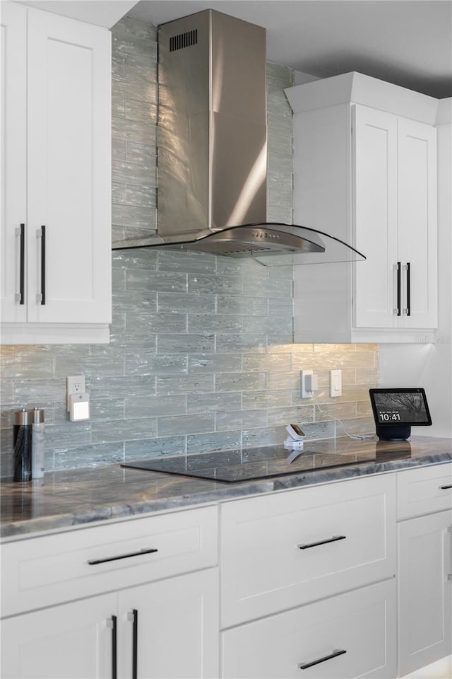 kitchen featuring dark stone countertops, white cabinets, decorative backsplash, and wall chimney exhaust hood