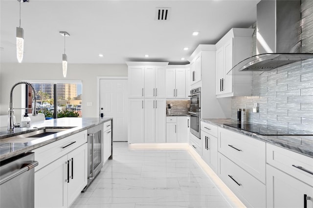 kitchen featuring wall chimney range hood, sink, appliances with stainless steel finishes, white cabinetry, and decorative light fixtures