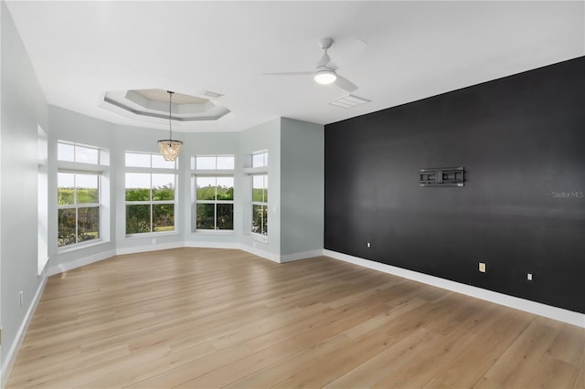 empty room with a raised ceiling, ceiling fan, and light hardwood / wood-style floors