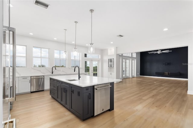 kitchen with sink, a kitchen island with sink, decorative light fixtures, stainless steel dishwasher, and french doors