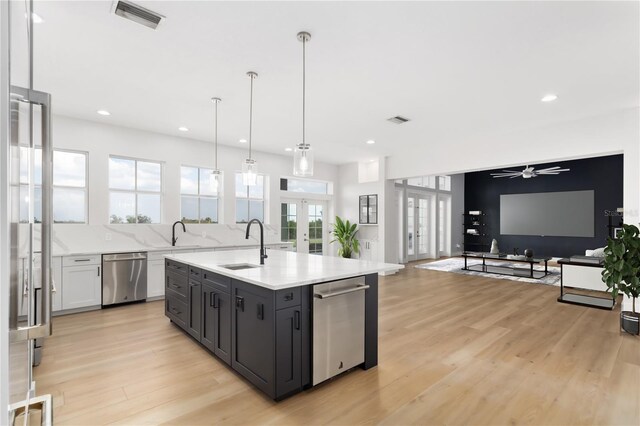 kitchen featuring pendant lighting, sink, a kitchen island with sink, stainless steel dishwasher, and french doors