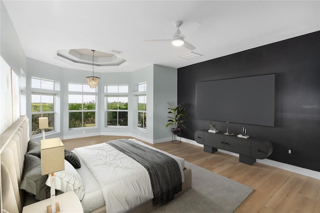 bedroom with ceiling fan, light wood-type flooring, and a tray ceiling