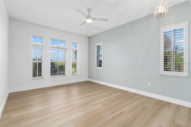 empty room with ceiling fan with notable chandelier and light hardwood / wood-style flooring