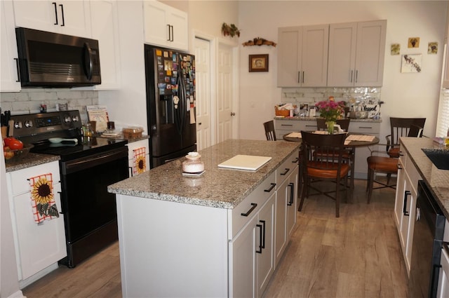 kitchen with a kitchen island, backsplash, white cabinets, light hardwood / wood-style floors, and black appliances