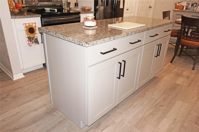 kitchen featuring black fridge, white cabinetry, stainless steel electric range, a kitchen island, and stone counters