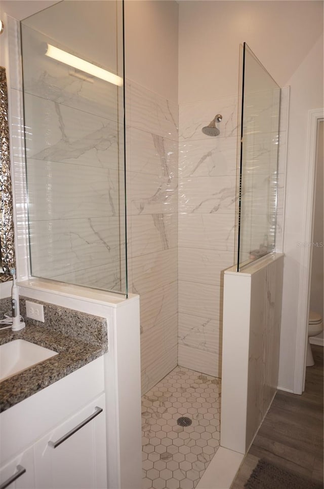 bathroom featuring a tile shower, vanity, and toilet