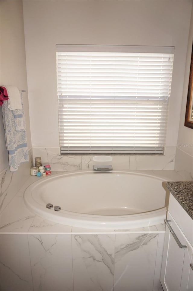 bathroom featuring a relaxing tiled tub, a healthy amount of sunlight, and vanity