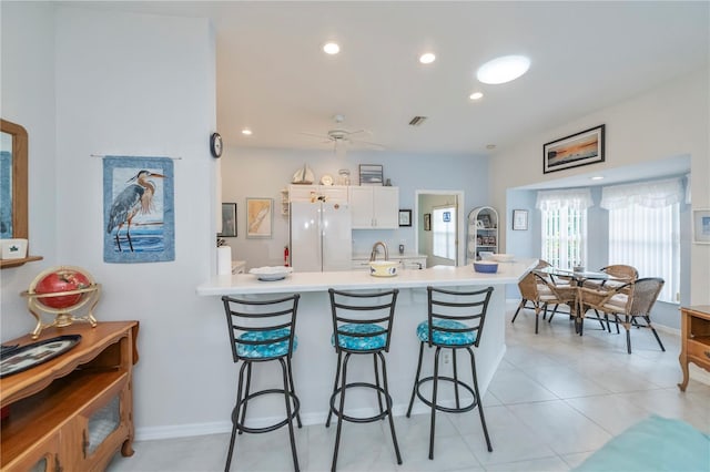 kitchen with a kitchen breakfast bar, kitchen peninsula, white fridge, and white cabinets