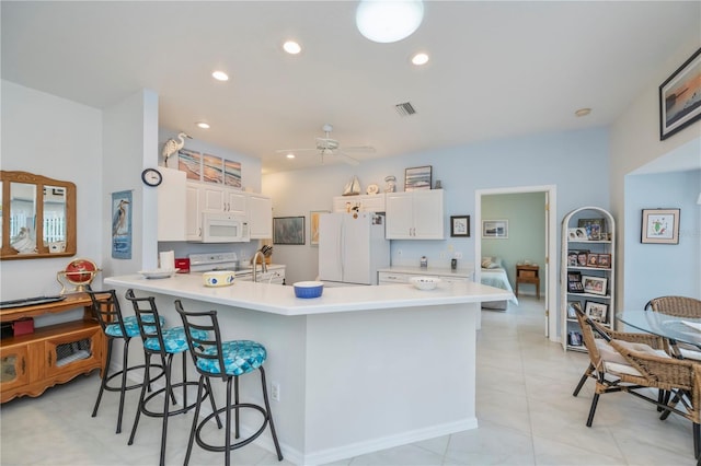 kitchen with white appliances, ceiling fan, white cabinetry, a kitchen bar, and kitchen peninsula