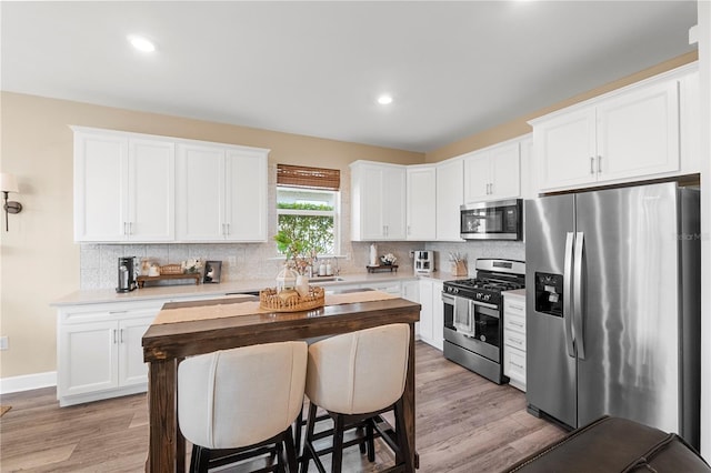 kitchen featuring backsplash, stainless steel appliances, light hardwood / wood-style floors, and white cabinets