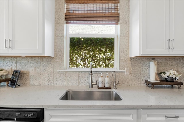 kitchen with light stone counters, sink, white cabinets, and dishwasher