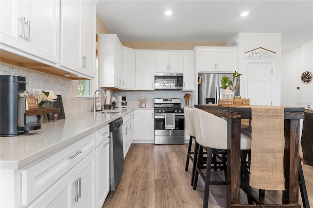 kitchen featuring sink, backsplash, white cabinets, light stone counters, and stainless steel appliances