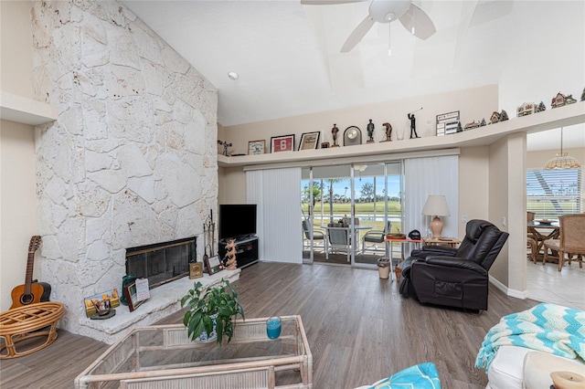 living room featuring hardwood / wood-style flooring, ceiling fan, a stone fireplace, and high vaulted ceiling