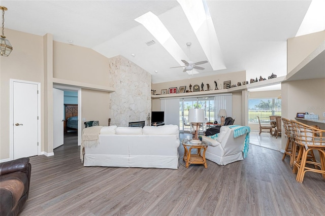 living room with hardwood / wood-style flooring, a stone fireplace, a skylight, and high vaulted ceiling