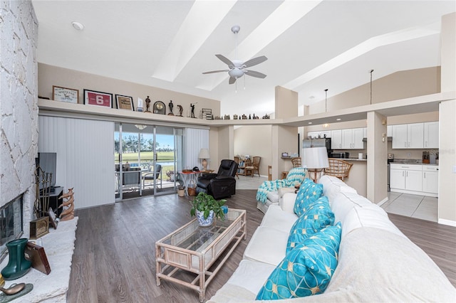 living room with ceiling fan, a large fireplace, vaulted ceiling, and light hardwood / wood-style flooring