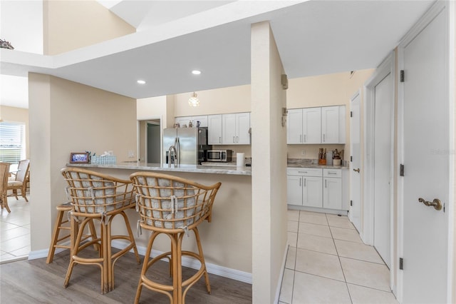 kitchen featuring light tile patterned flooring, a kitchen bar, kitchen peninsula, stainless steel appliances, and white cabinets