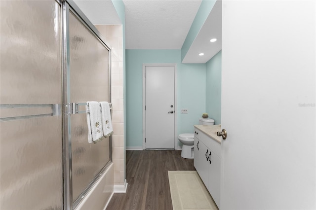 full bathroom featuring enclosed tub / shower combo, vanity, wood-type flooring, a textured ceiling, and toilet