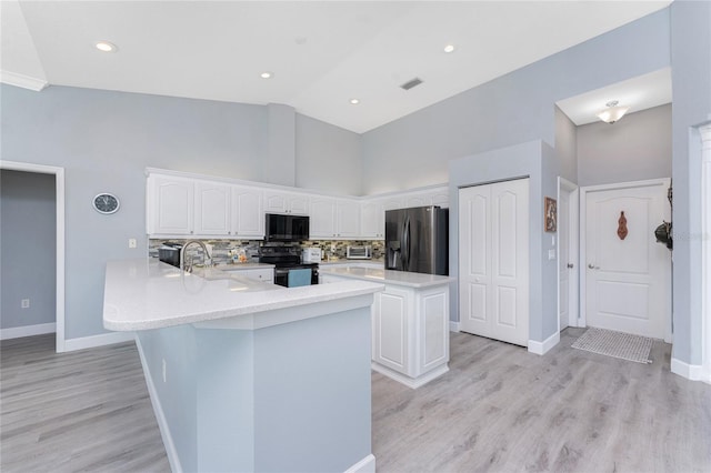 kitchen featuring white cabinets, decorative backsplash, a peninsula, black appliances, and a sink