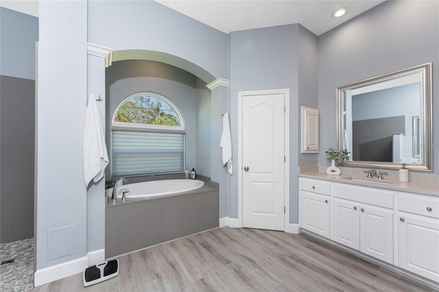 full bathroom featuring baseboards, wood finished floors, vanity, a bath, and recessed lighting