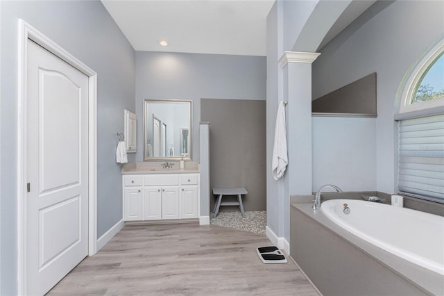 bathroom with decorative columns, baseboards, wood finished floors, a garden tub, and vanity