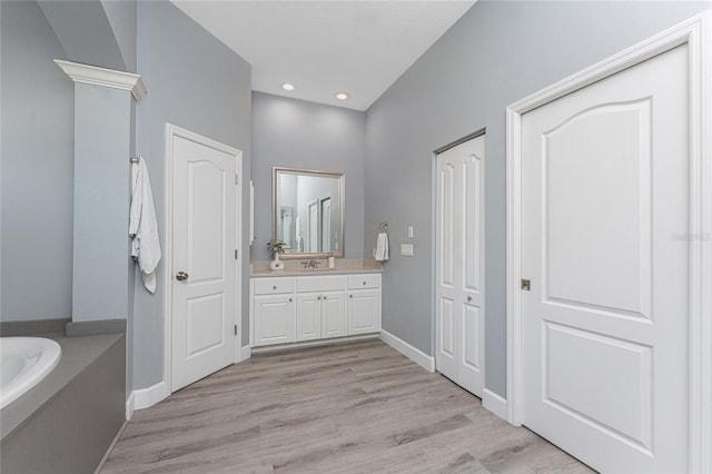 bathroom featuring a bath, wood finished floors, a closet, and vanity