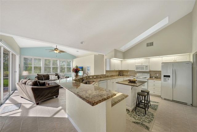 kitchen with a breakfast bar, sink, light tile patterned floors, kitchen peninsula, and white appliances