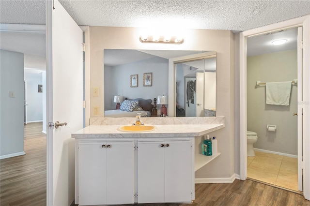 bathroom with hardwood / wood-style flooring, vanity, toilet, and a textured ceiling