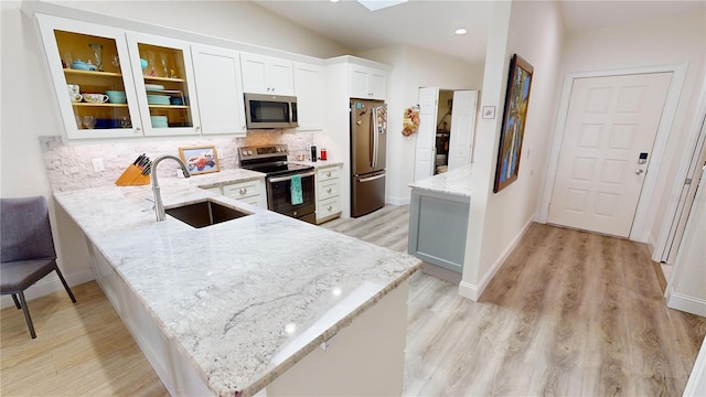 kitchen with sink, light stone counters, kitchen peninsula, stainless steel appliances, and white cabinets