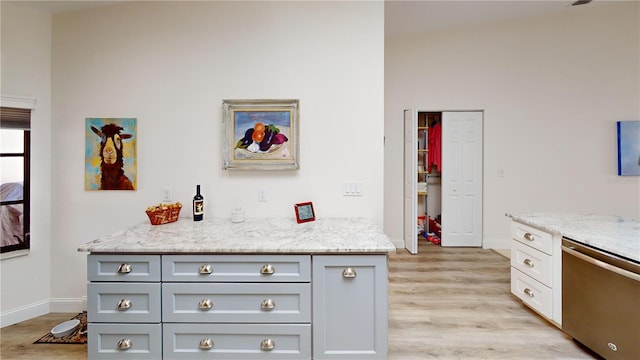 kitchen featuring stainless steel dishwasher, gray cabinets, light stone countertops, and light wood-type flooring