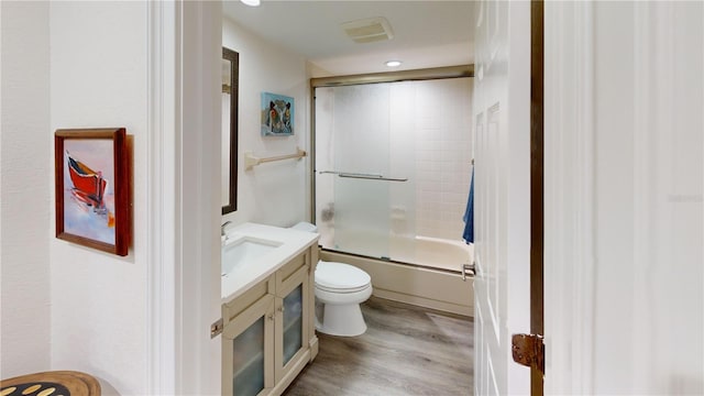 full bathroom with enclosed tub / shower combo, hardwood / wood-style floors, vanity, and toilet