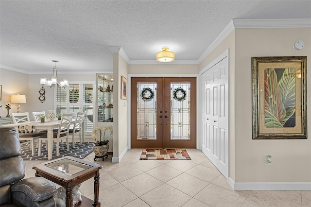 tiled entrance foyer with french doors, ornamental molding, an inviting chandelier, and a textured ceiling