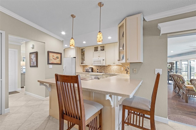 kitchen with pendant lighting, white appliances, ornamental molding, a kitchen bar, and decorative backsplash