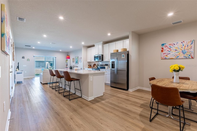 kitchen featuring appliances with stainless steel finishes, a breakfast bar area, white cabinets, light hardwood / wood-style floors, and a center island with sink