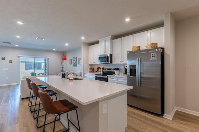 kitchen featuring stainless steel appliances, an island with sink, light hardwood / wood-style flooring, and white cabinets