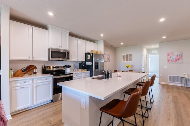 kitchen with a breakfast bar, sink, a center island with sink, stainless steel appliances, and white cabinets