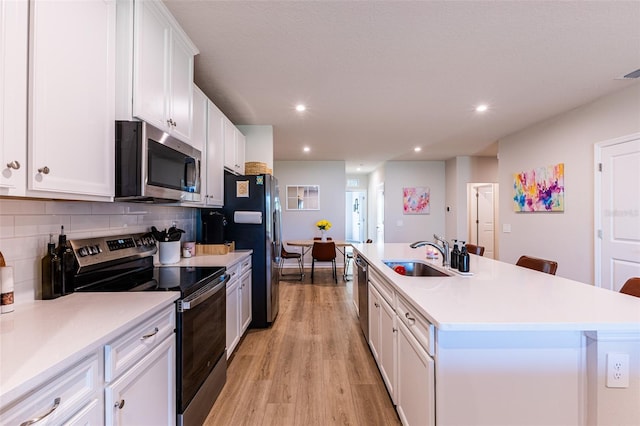 kitchen with appliances with stainless steel finishes, a kitchen island with sink, sink, and white cabinets