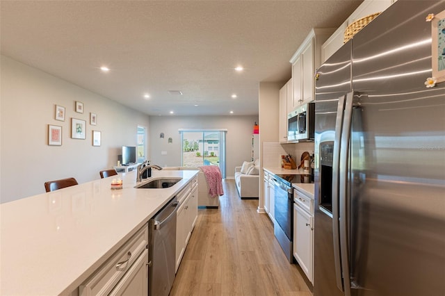 kitchen with sink, light hardwood / wood-style flooring, appliances with stainless steel finishes, a kitchen breakfast bar, and white cabinets