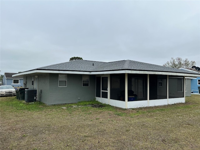 back of property with central air condition unit, a sunroom, roof with shingles, and a yard