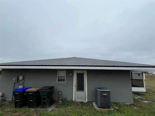 rear view of house with a shingled roof, central AC, and stucco siding