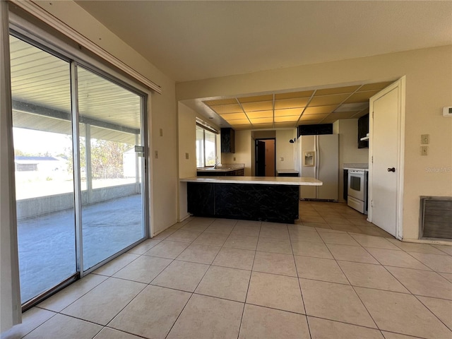 kitchen with light tile patterned floors, a peninsula, white appliances, visible vents, and light countertops