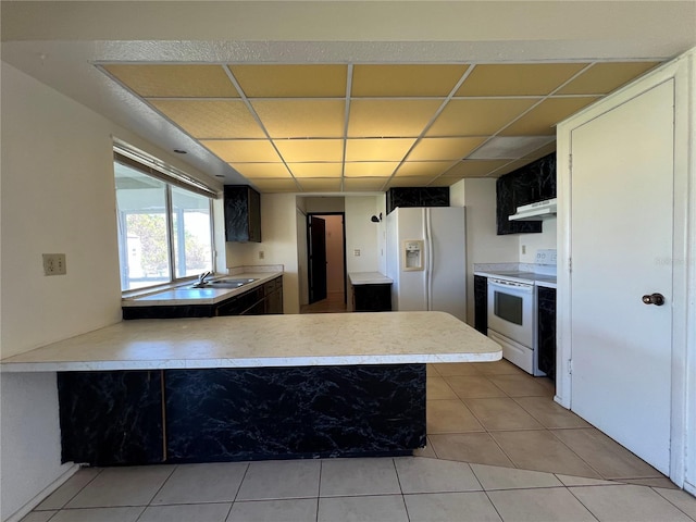 kitchen featuring a drop ceiling, under cabinet range hood, a peninsula, white appliances, and a sink