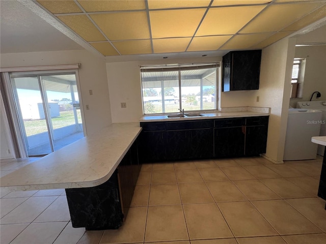 kitchen featuring light countertops, a sink, washer / dryer, plenty of natural light, and a peninsula