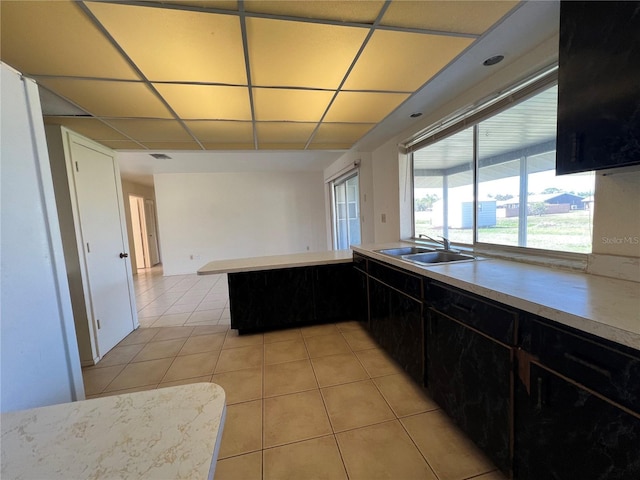 kitchen featuring light tile patterned floors, a paneled ceiling, light countertops, a sink, and dark cabinetry