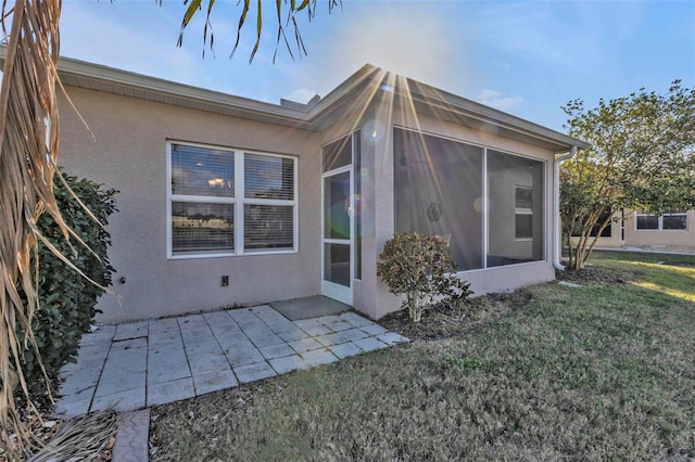 back of property with a lawn, a sunroom, and a patio