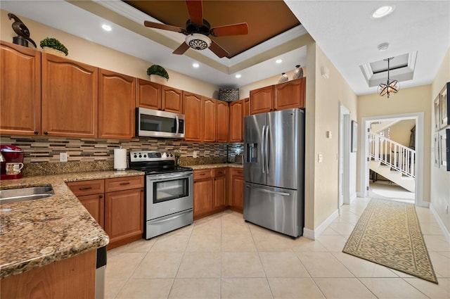 kitchen featuring pendant lighting, appliances with stainless steel finishes, backsplash, a tray ceiling, and light stone countertops